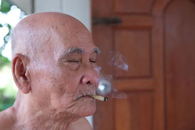 Shirtless senior man smoking cigarette while sitting outdoors