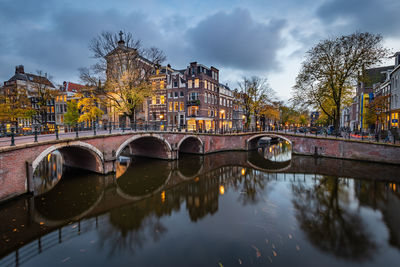 Bridge over river by buildings against sky