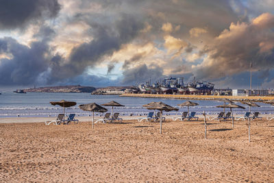 Beach chairs with parasols in row on sandy beach in sunny day against cloudy sky