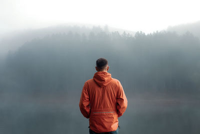 Man standing at lake during foggy weather 