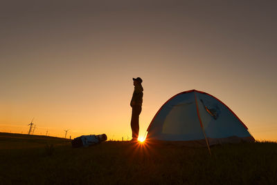 Man standing by tent against sky during sunset