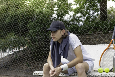 Portrait of young man looking to a tennis match while sitting on bench with a towel around his neck