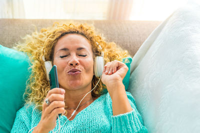 Mature woman listening music while lying down on sofa at home