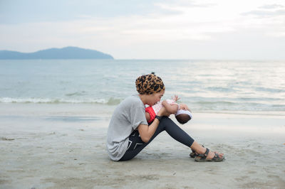 Full length of man sitting on shore at beach against sky