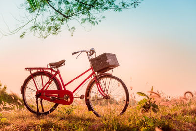 Bicycle parked on grassy field against sky during sunset