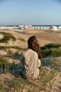 Rear view of woman sitting at beach against sky