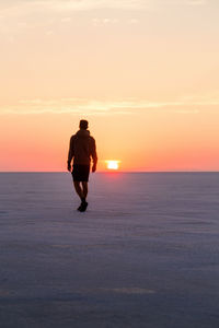 Rear view of man standing on beach against sky during sunset