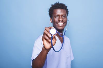 Portrait of young woman holding stethoscope against blue background