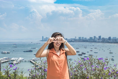 Portrait of woman gesturing heart shape against sky