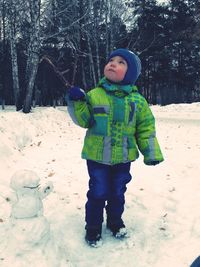 Full length of child standing by snowman against trees on field