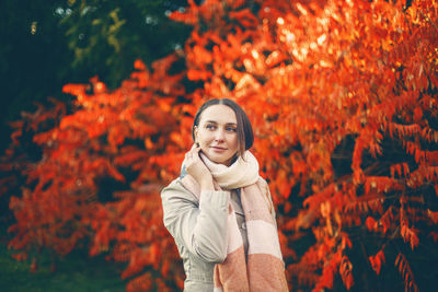 Beautiful woman standing against orange tree during autumn