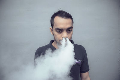 Man emitting smoke from nose while standing against gray background