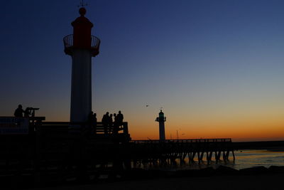 Silhouette built structure by sea against clear sky