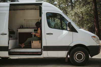 Side view of woman reading book while sitting in motor home at forest