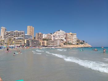 Buildings by sea against clear blue sky