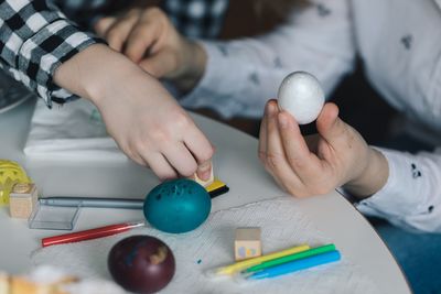 Cropped hands decorating easter egg on table