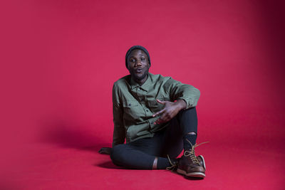 Portrait of young man sitting against pink background