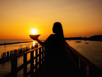 Silhouette man standing by railing against sea during sunset