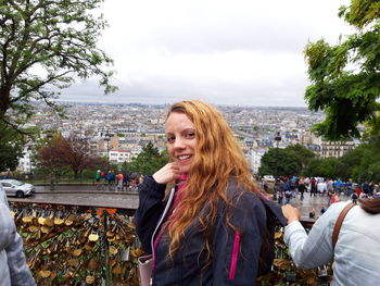 Portrait of smiling young woman standing in city against sky