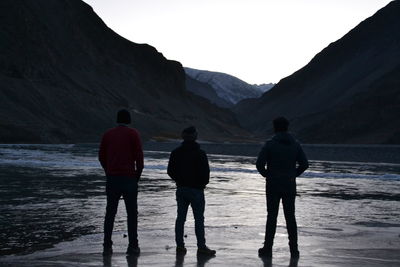Rear view of men standing by lake against mountains