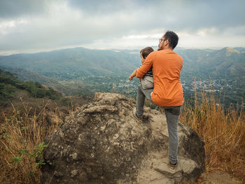 Rear view of man standing on mountain against sky