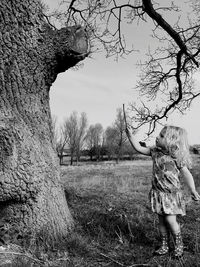 Girl standing by tree on field against sky