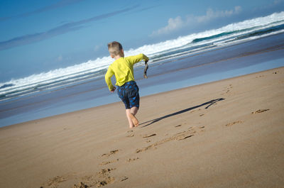 Full length of boy running on beach against sky