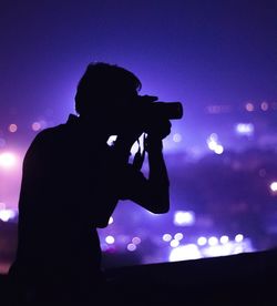 Silhouette of person photographing illuminated ferris wheel at night