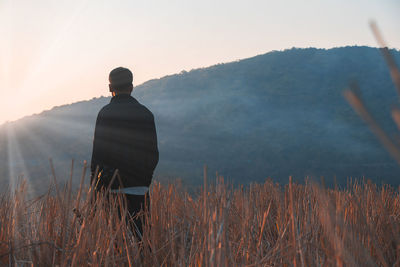 Rear view of man standing on field against sky