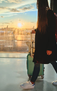 View on the aiport window with woman walking with suitcase at the departure hall during the sunset. 