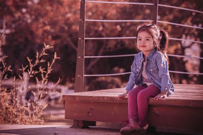 Full length of girl sitting on wooden walkway