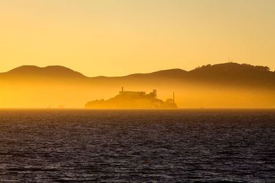 Scenic view of island in sea against orange sky