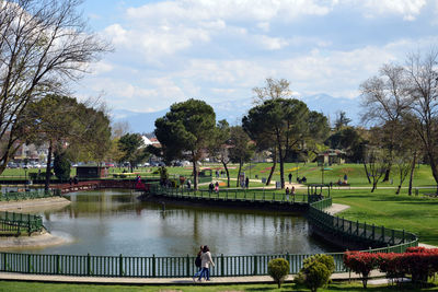 People in park by lake against sky