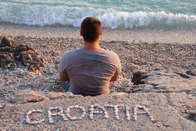 Croatia texts made by pebble behind man sitting at beach