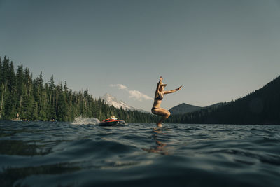 A young woman jumps from a paddle board into lost lake in oregon.