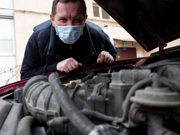 Portrait of man wearing mask examining car engine