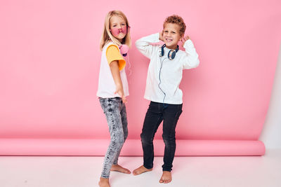 Portrait of sibling wearing headphones against colored background