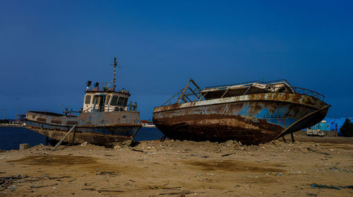Abandoned boat on beach against blue sky
