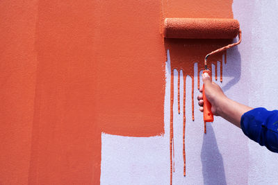 Midsection of man holding umbrella against orange wall