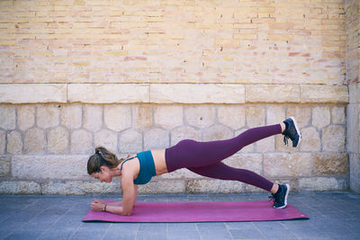 Full length of woman with arms raised against brick wall