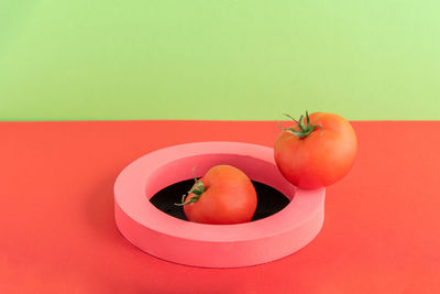 Tomatoes come out from the hole through a pink ring on a green and red background. 