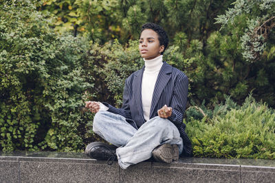 Thoughtful young businesswoman looking away while practicing yoga on retaining wall