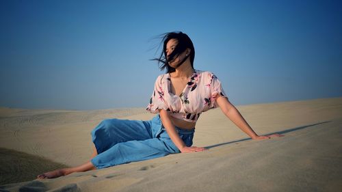 Beautiful woman sitting on sand in dessert against sky