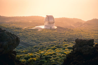High angle of breathtaking landscape with observatory located on hill above clouds at sunset