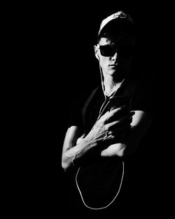 Young man listening music while standing against black background