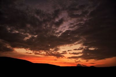 Silhouette landscape against dramatic sky during sunset