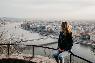 Woman standing by railing against bridge in city against sky