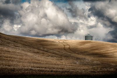 Distant view of silo on agricultural field against cloudy sky