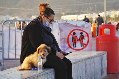 Woman using mobile phone with dog sitting outdoors