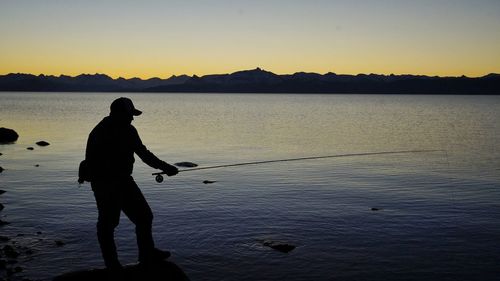 Silhouette man fishing in lake against sky during sunset